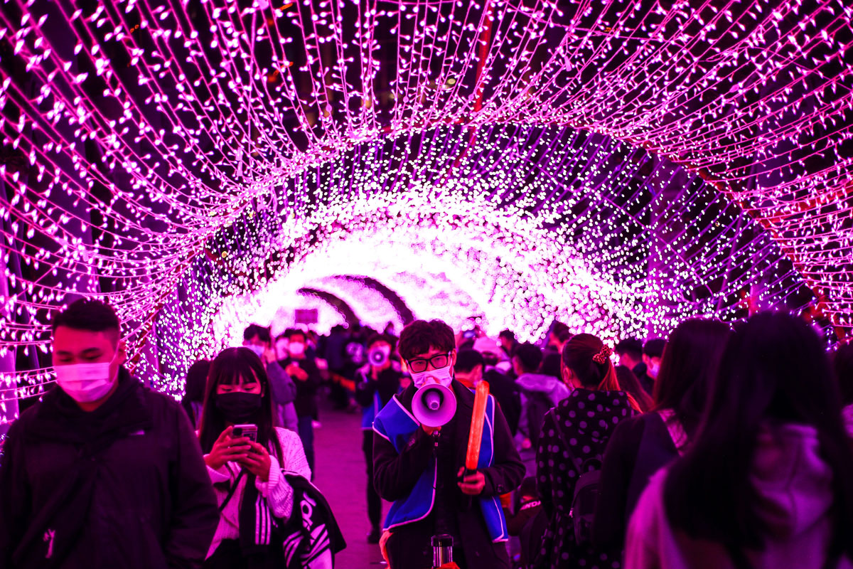 A volunteer speaks through a megaphone to remind people to wear a mask while walking under Christmas decorations in New Taipei City, Taiwan on December 18.