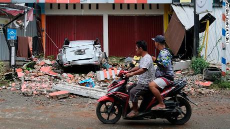 Motorists ride past the wreckage of a car damaged in an earthquake in Mamuju, West Sulawesi, Indonesia.