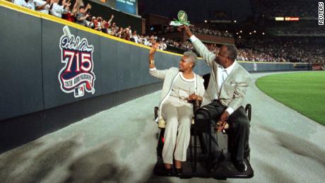 Aaron and his wife, Billye, wave to fans as they pass a sign honoring Aaron on the outfield wall at Turner Field after a ceremony honoring the 25th anniversary of Aaron&#39;s record-breaking home run.