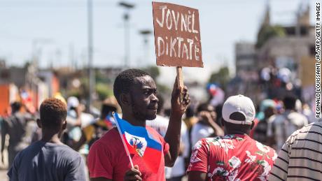 People hold up signs during a demonstration on February 14, 2021 in  Port-au-Prince.