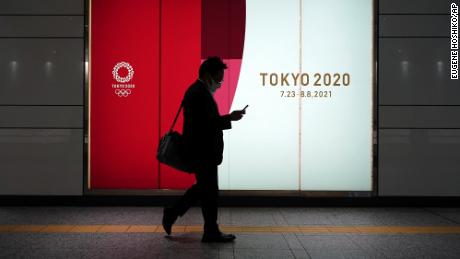 A man wearing a protective mask to help curb the spread of the coronavirus walks near advertisement for Tokyo 2020 Olympics at an underpass Tuesday, April 6, in Tokyo.