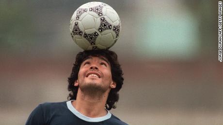 Argentine soccer star Diego Maradona, wearing a diamond earring, balances a soccer ball on his head as he walks off the practice field following the national selection&#39;s May 22, 1986 practice session in Mexico City.